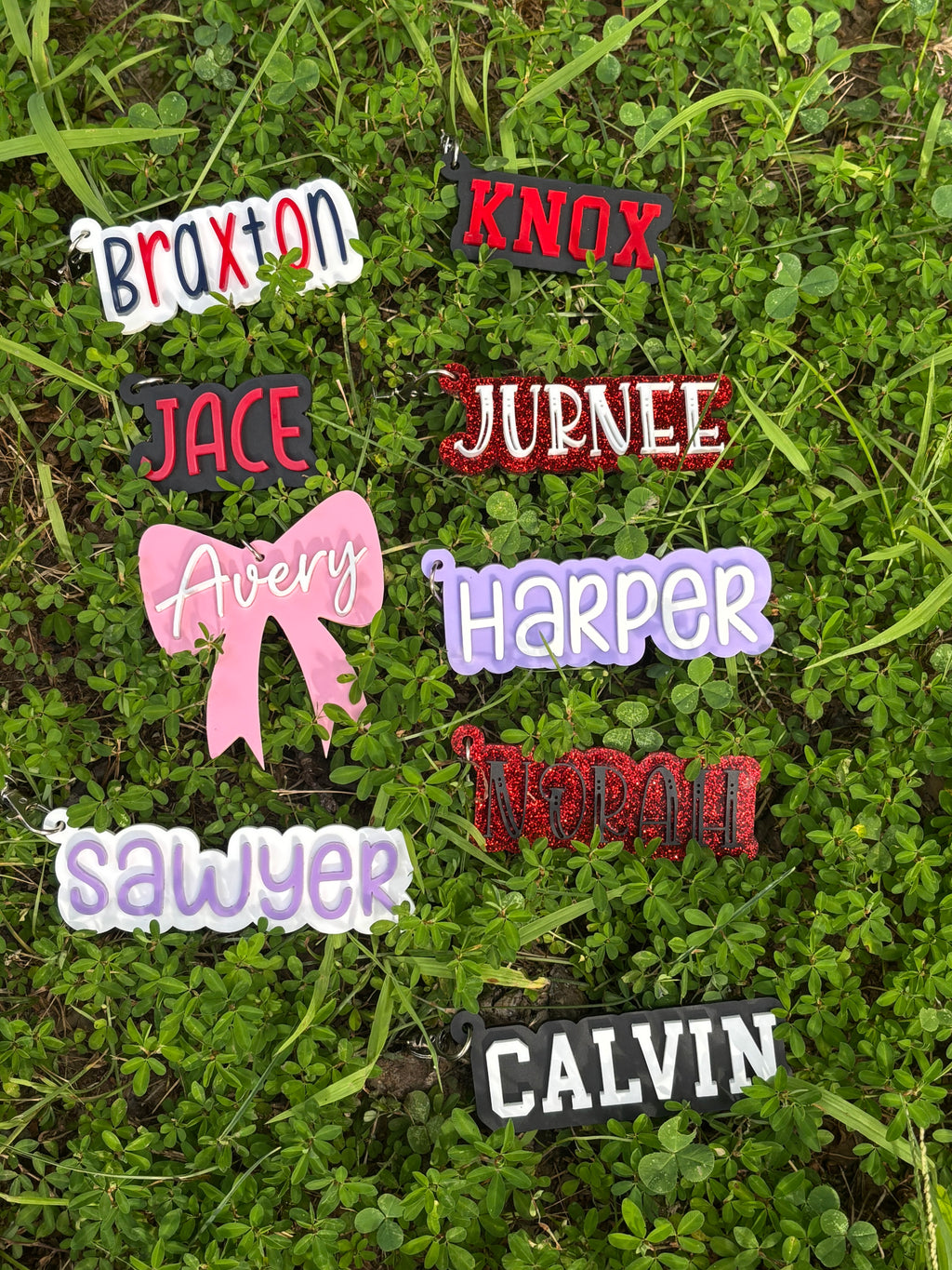 Acrylic name keychains on grass with names Braxton, Knox, Jace, Journee, Avery, and Harper