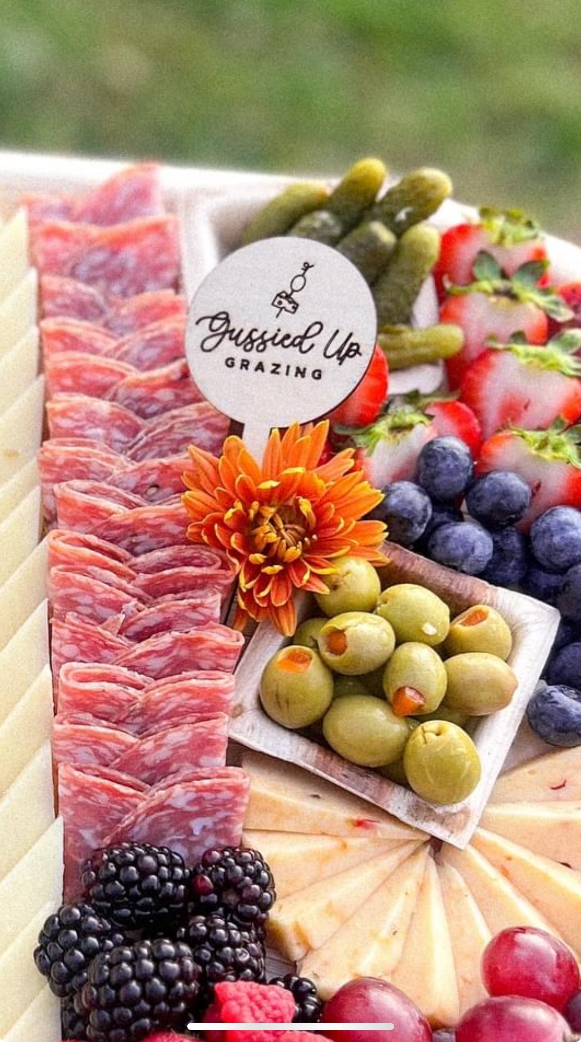 Engraved charcuterie board with cured meat, olives, berries, flower and round label