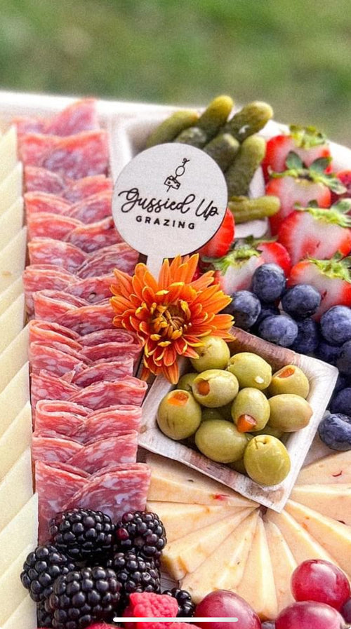 Engraved charcuterie board with cured meat, olives, berries, flower and round label