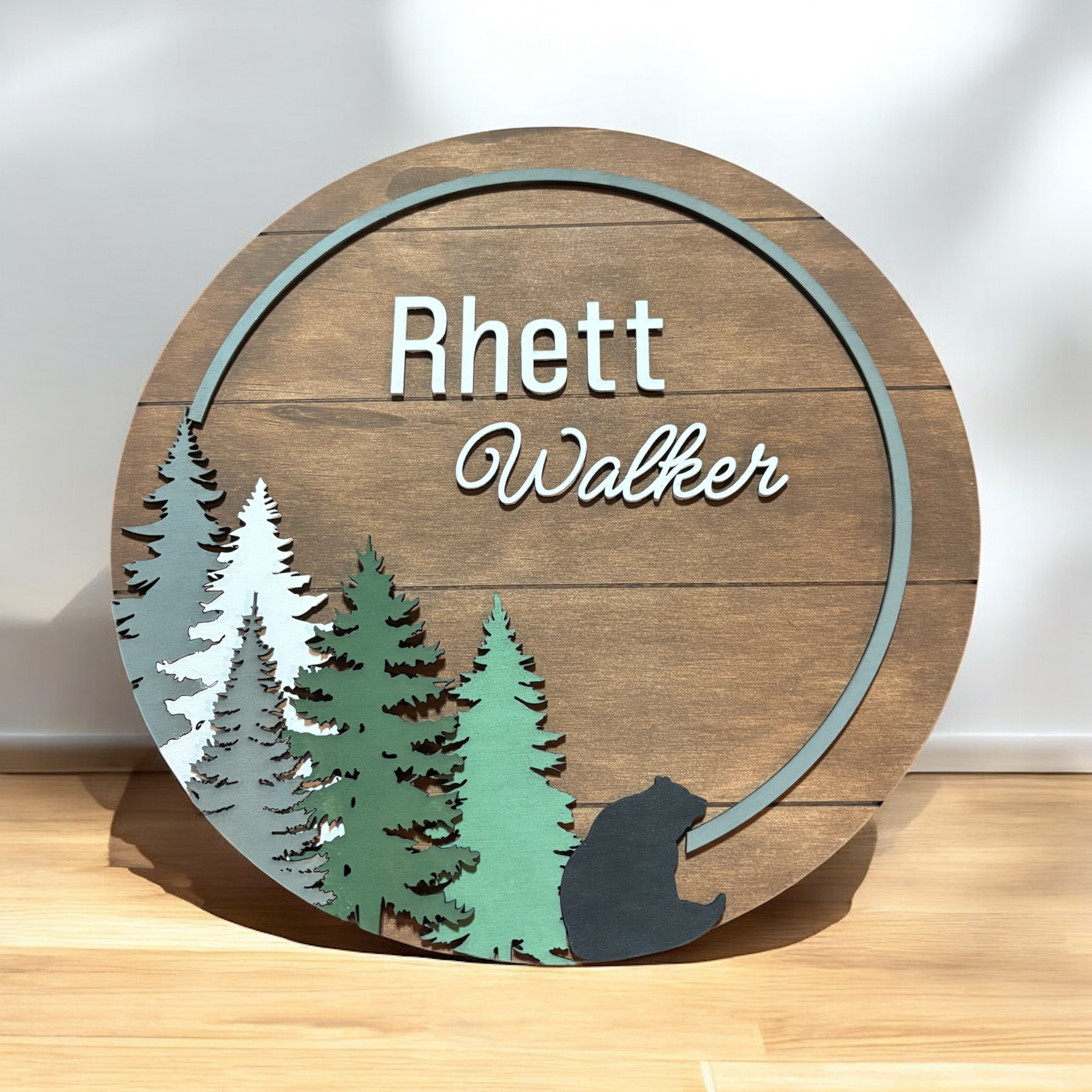 Round wooden name sign with forest trees, bear silhouette, and Rhett Walther