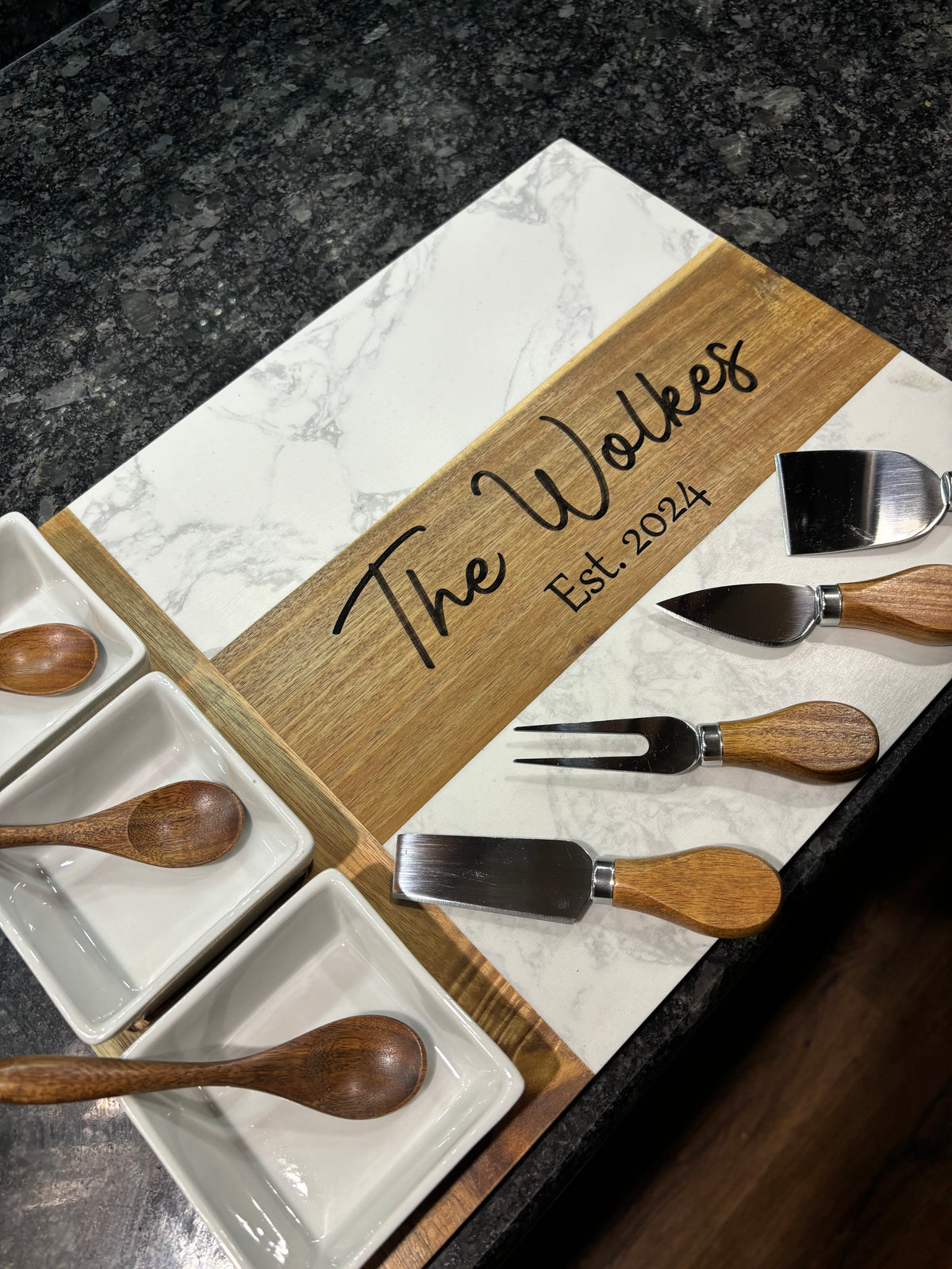 Charcuterie serving set with marble board, wooden utensils, and three white serving bowls