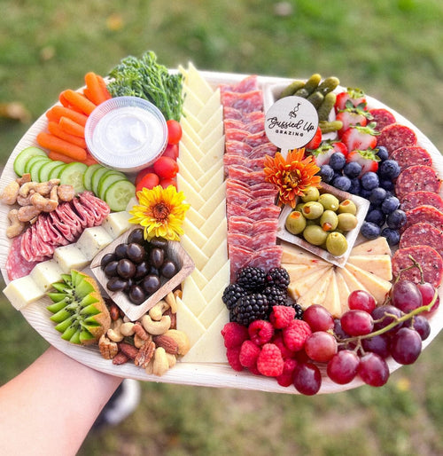 Engraved charcuterie board with assorted fruits, carrots, cured meats, olives and round label