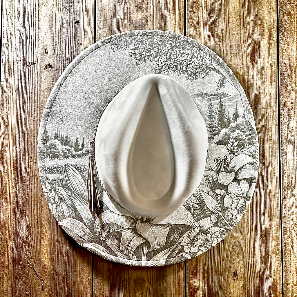 Gray suede fedora-style hat with white brim lining and engraved forest pattern